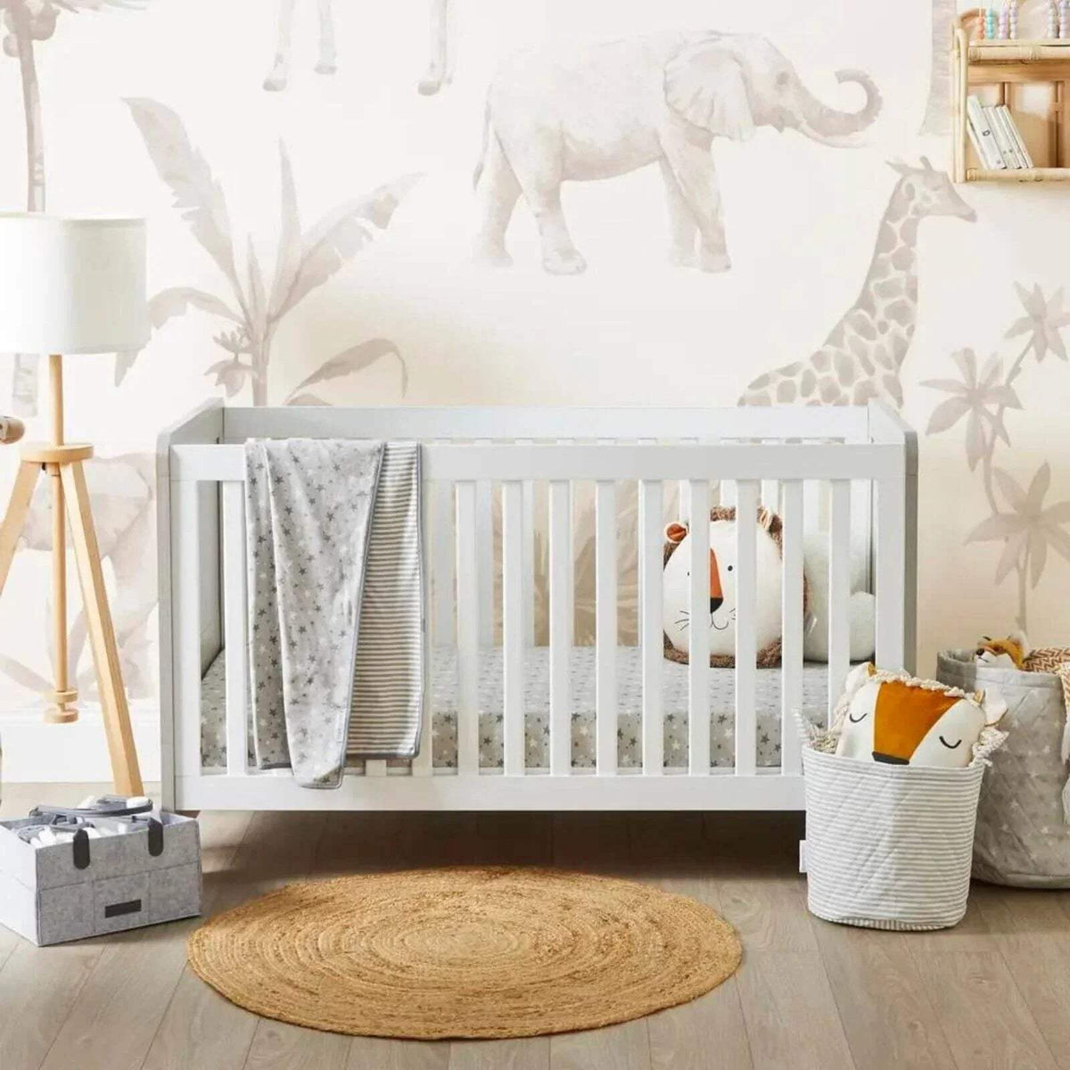 Ash grey cot bed with white slats, fitted sheet and folded blanket inside