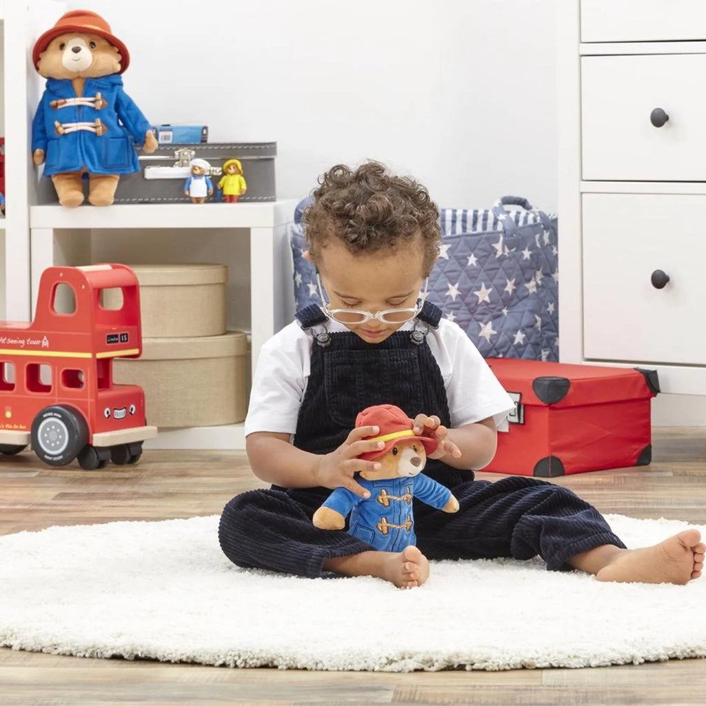 Paddington plush bear toy in child’s hands, red hat and blue coat