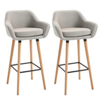 Set of 2 beige upholstered bar stools with curved seats, wood legs, and black metal footrests