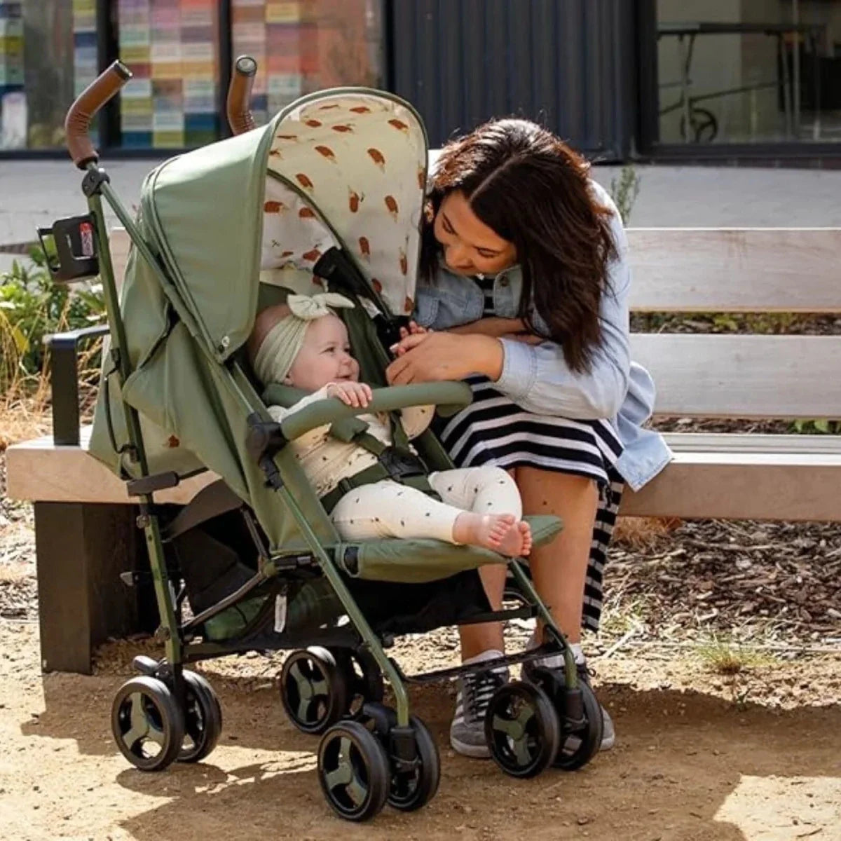 Green patterned stroller with seated baby and canopy, three-wheel design