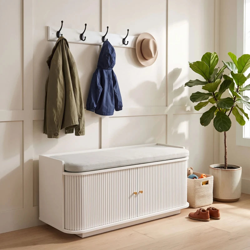 White hallway storage bench with wall coat hooks, padded seat, and shoe storage cabinet