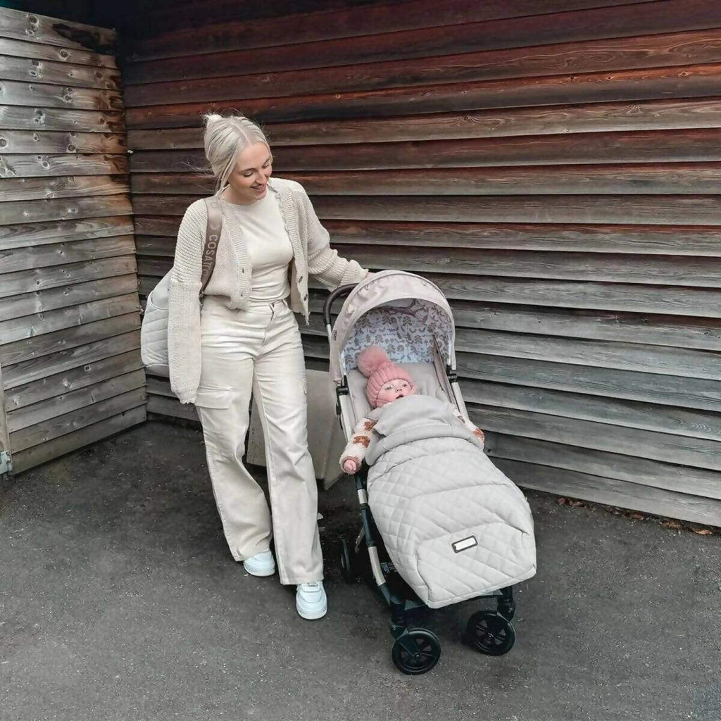 Gray stroller with infant inside, parent standing beside it outdoors
