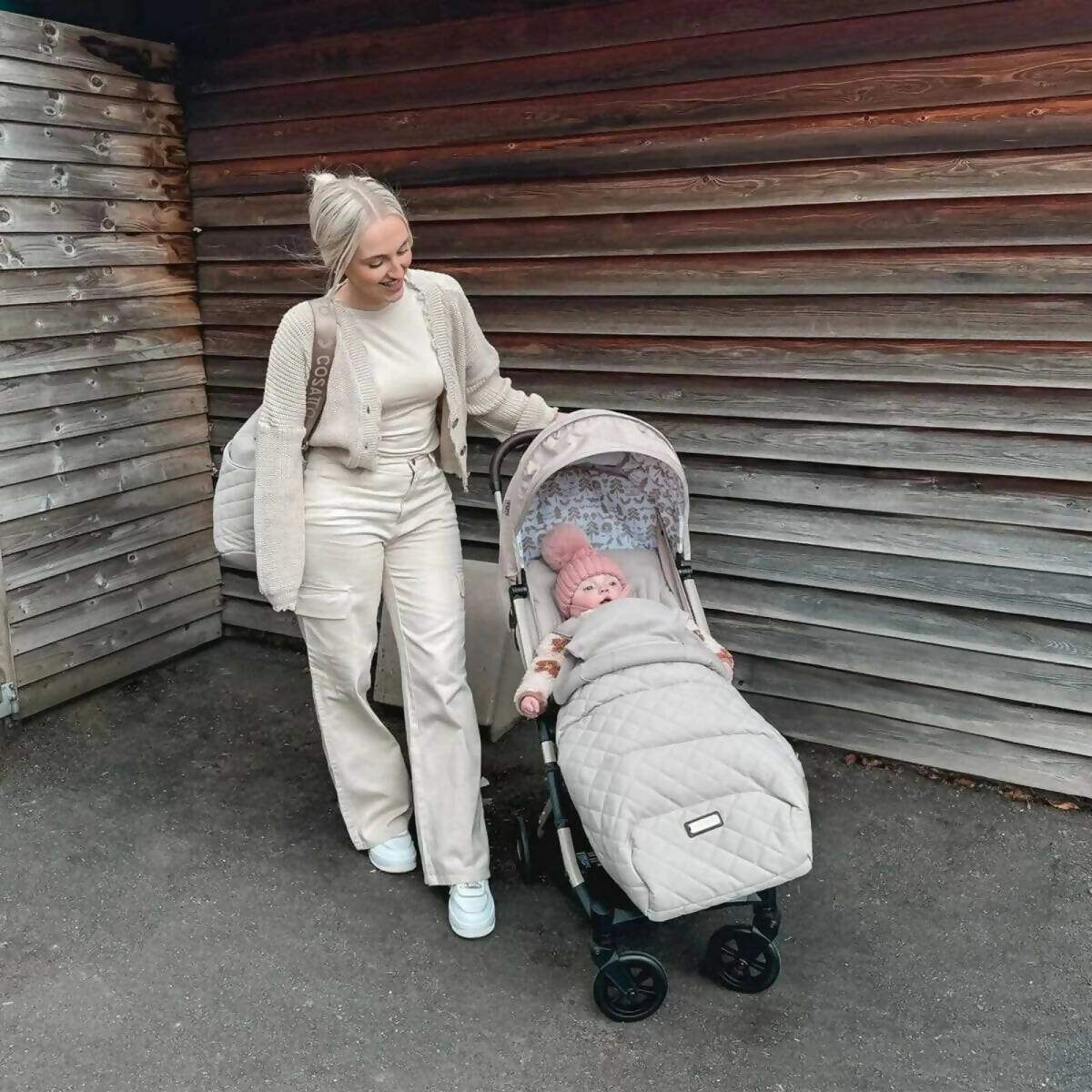 Gray stroller with infant inside, parent standing beside it outdoors