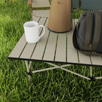 Close-up of khaki slatted tabletop on aluminum folding frame with carry bag beside it