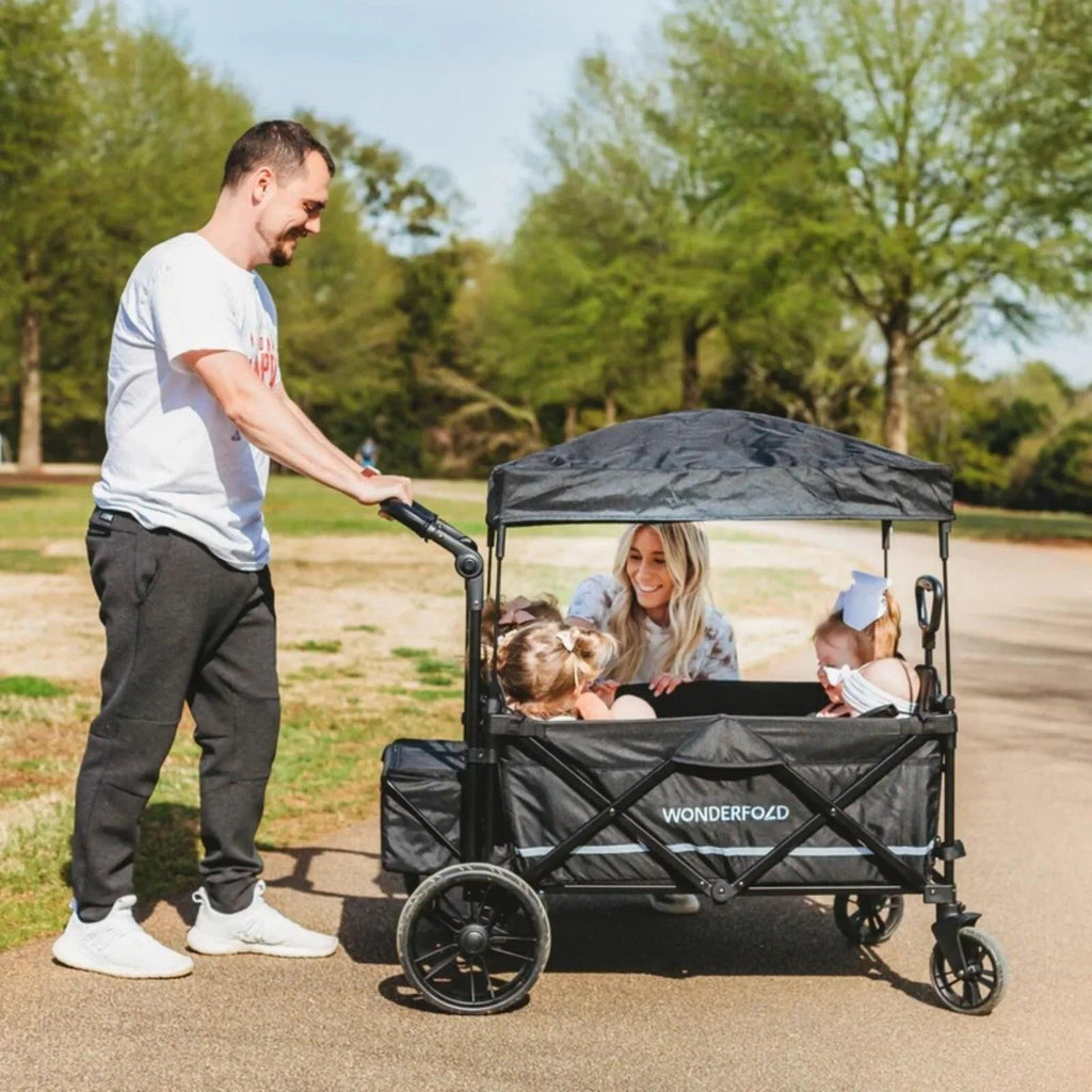 Black quad stroller wagon with canopy and safety seats, being pushed along a path