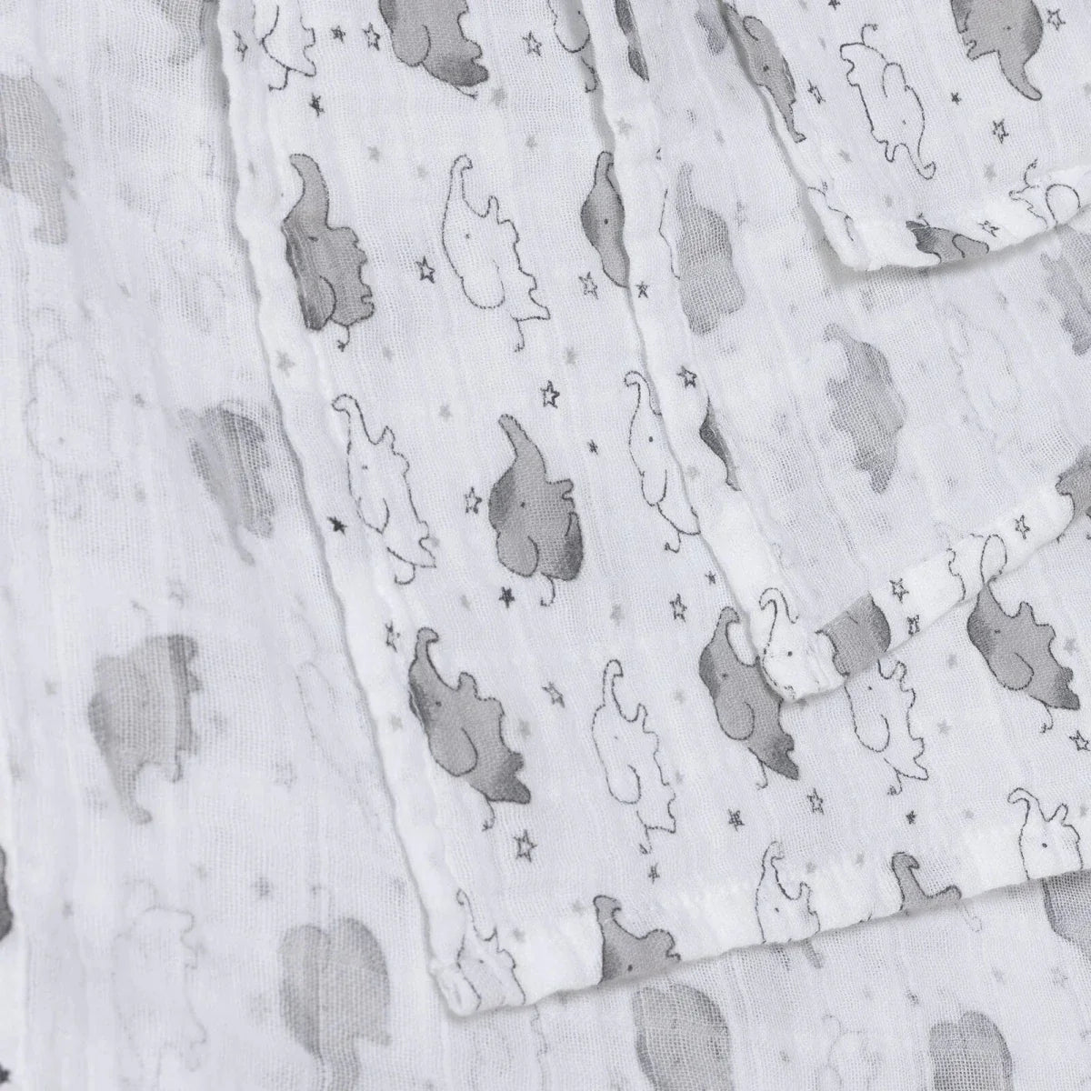 White muslin baby blanket with gray elephants and small stars, visible fabric texture