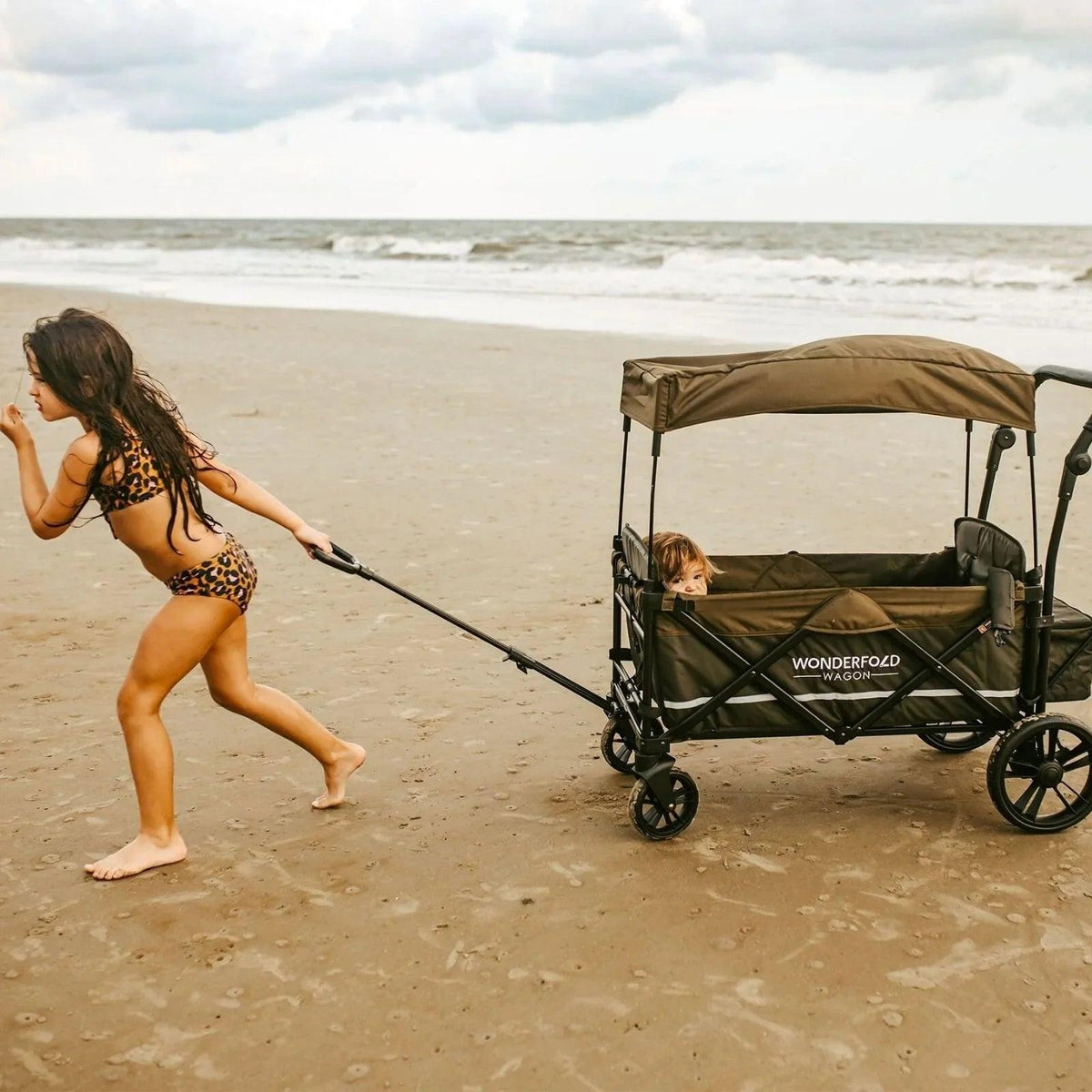 Dark navy quad stroller wagon with canopy on beach, pushed along sand