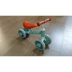 Green toddler balance bike with orange seat, white handlebar and four silent EVA wheels