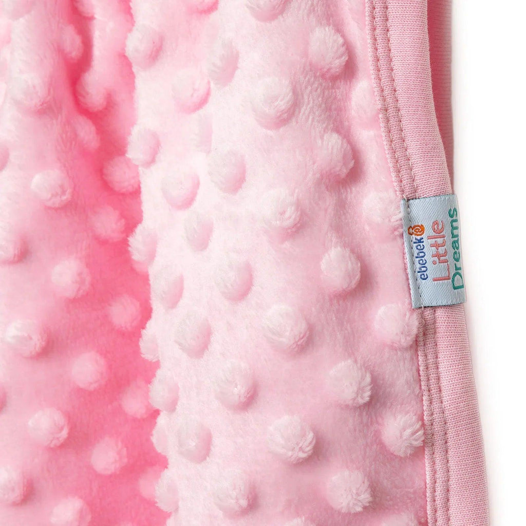 Pink fleece baby blanket label at stitched border with raised dot texture.