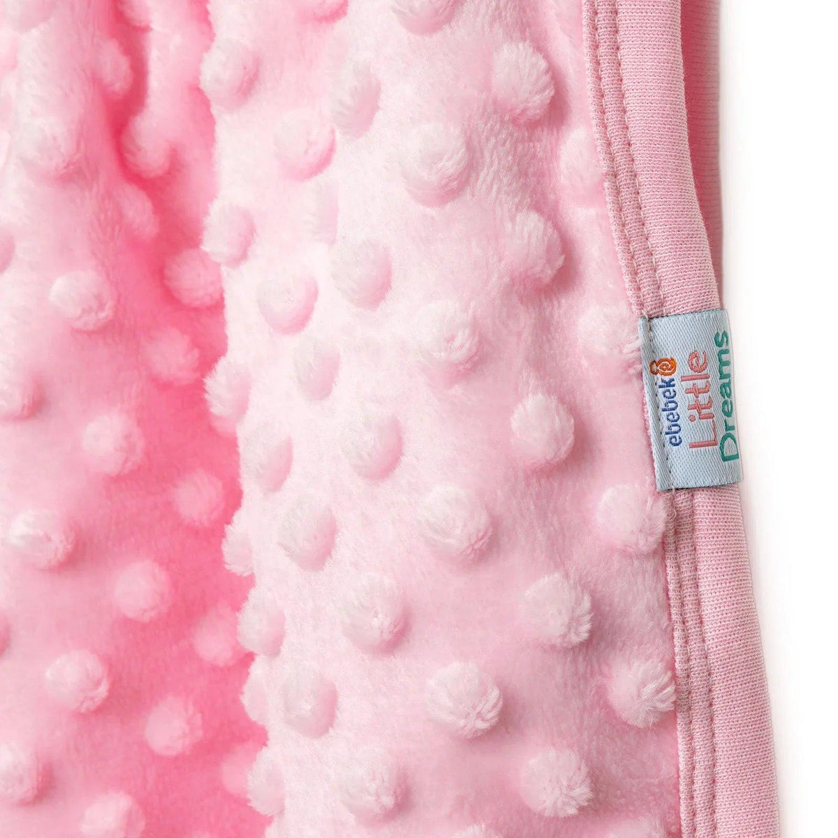 Pink fleece baby blanket label at stitched border with raised dot texture.
