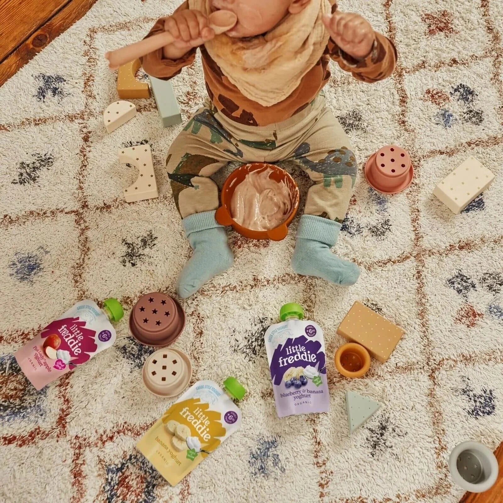 Baby food pouches scattered on a play mat, Little Freddie packaging with green caps