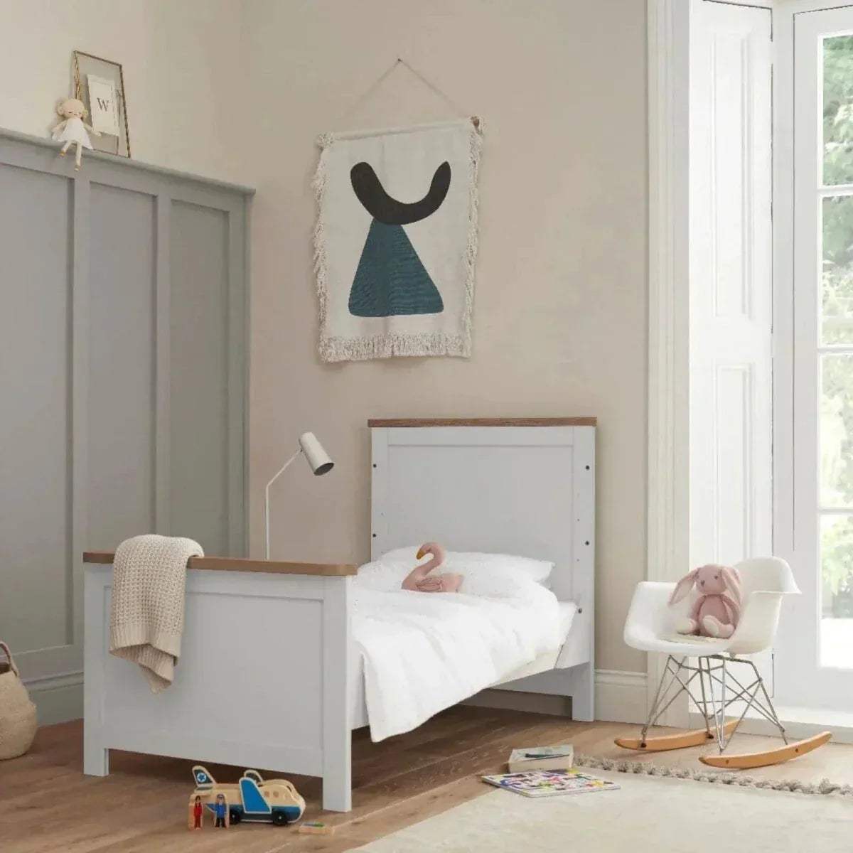 White cot bed with slatted rails and oak top rail, styled with white bedding