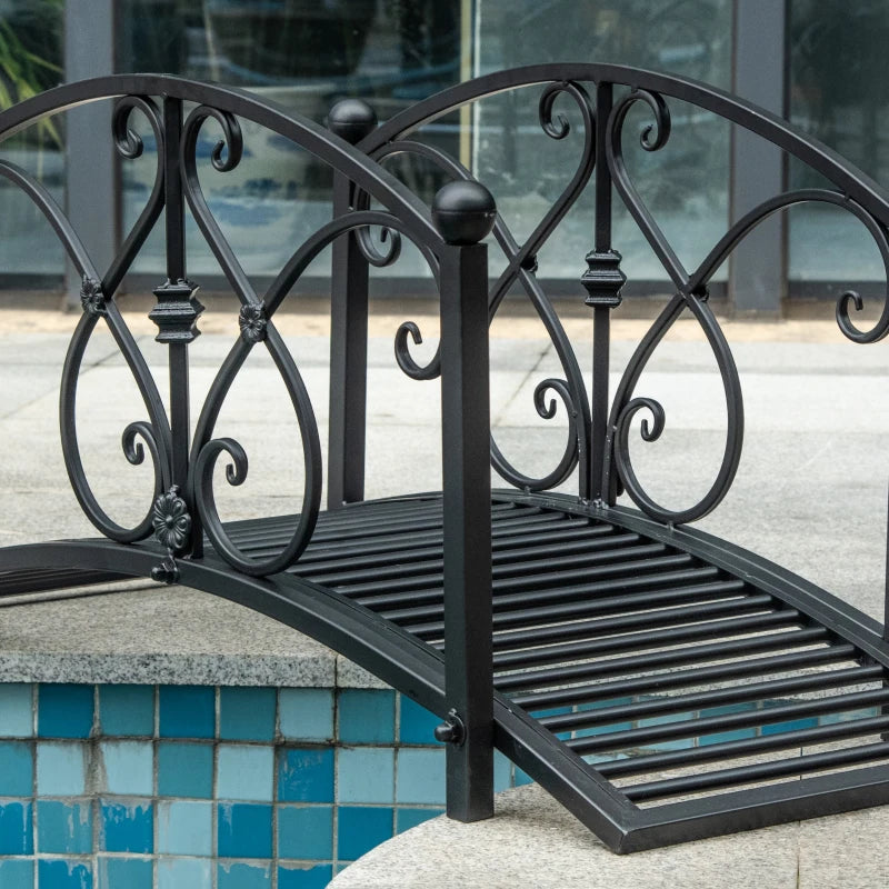 Black metal bridge with arched scroll railings and slatted walkway near water
