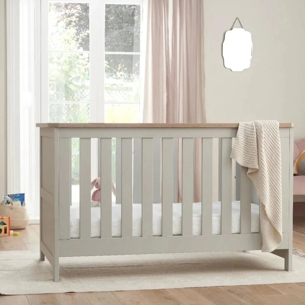 White and dove grey cot bed with vertical slats and oak top rail, with folded blanket