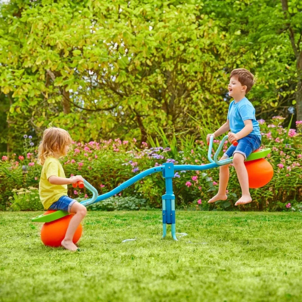 Children using a blue hop seesaw with orange ball seats in a garden