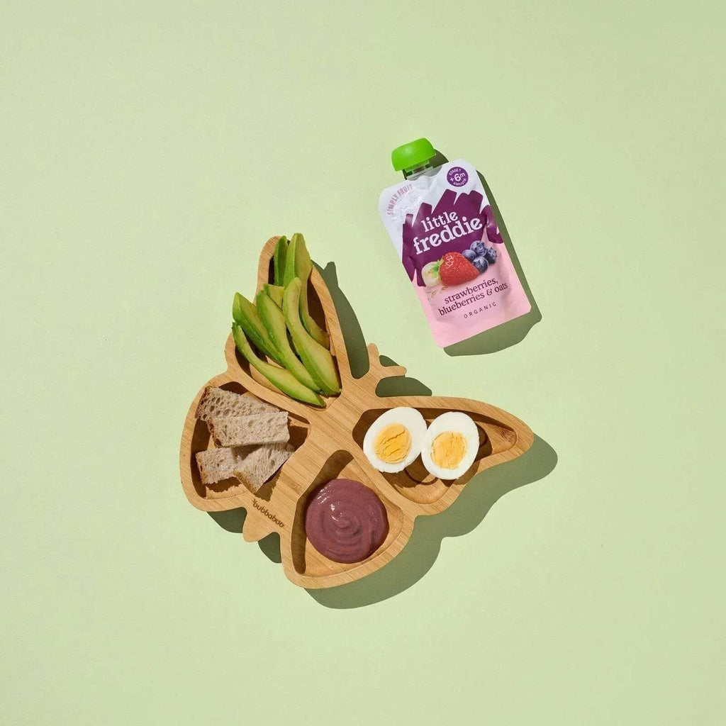 Baby food pouch with green cap on wooden food board, purple pouch