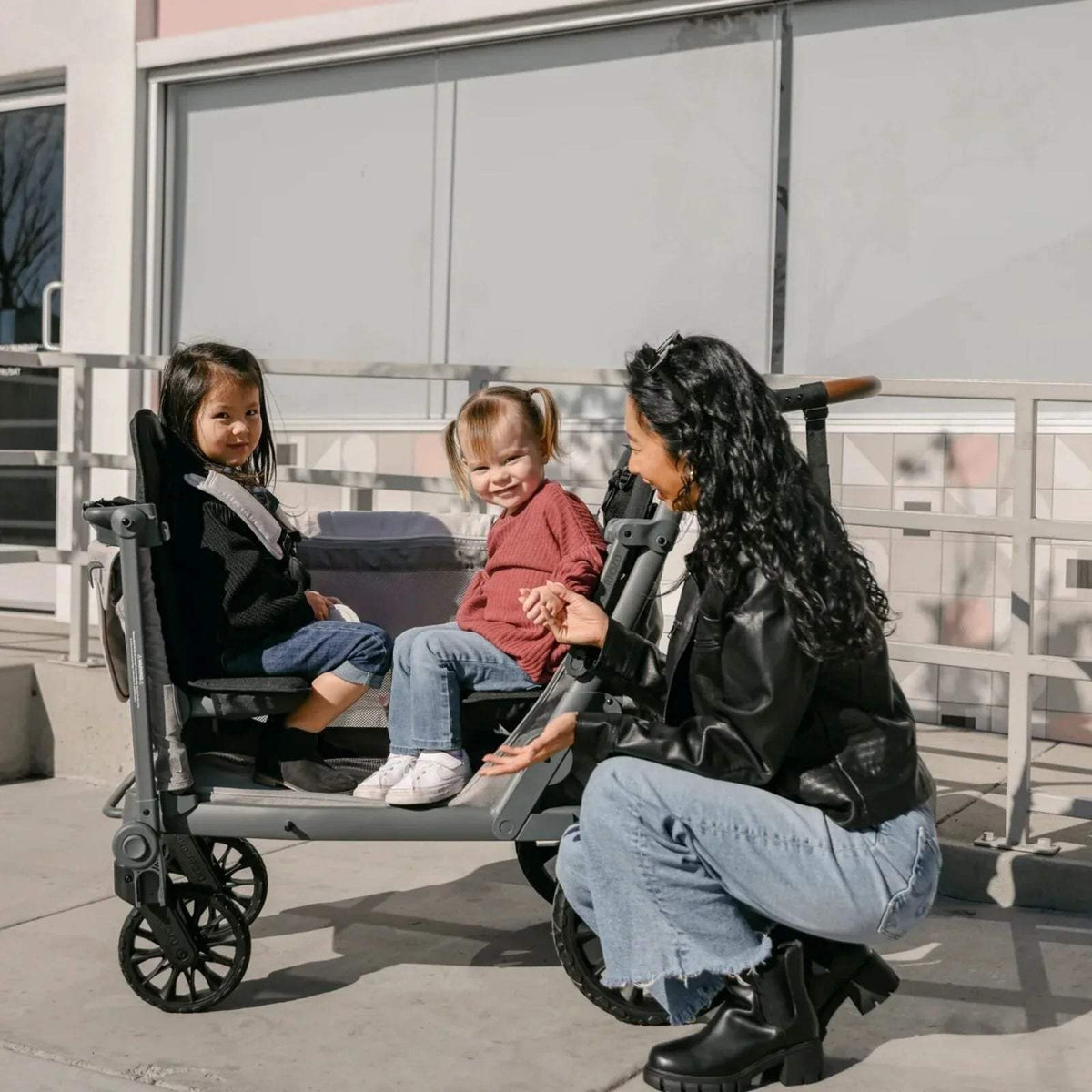 Black quad stroller wagon with canopy, toddler and child seated as a caregiver kneels