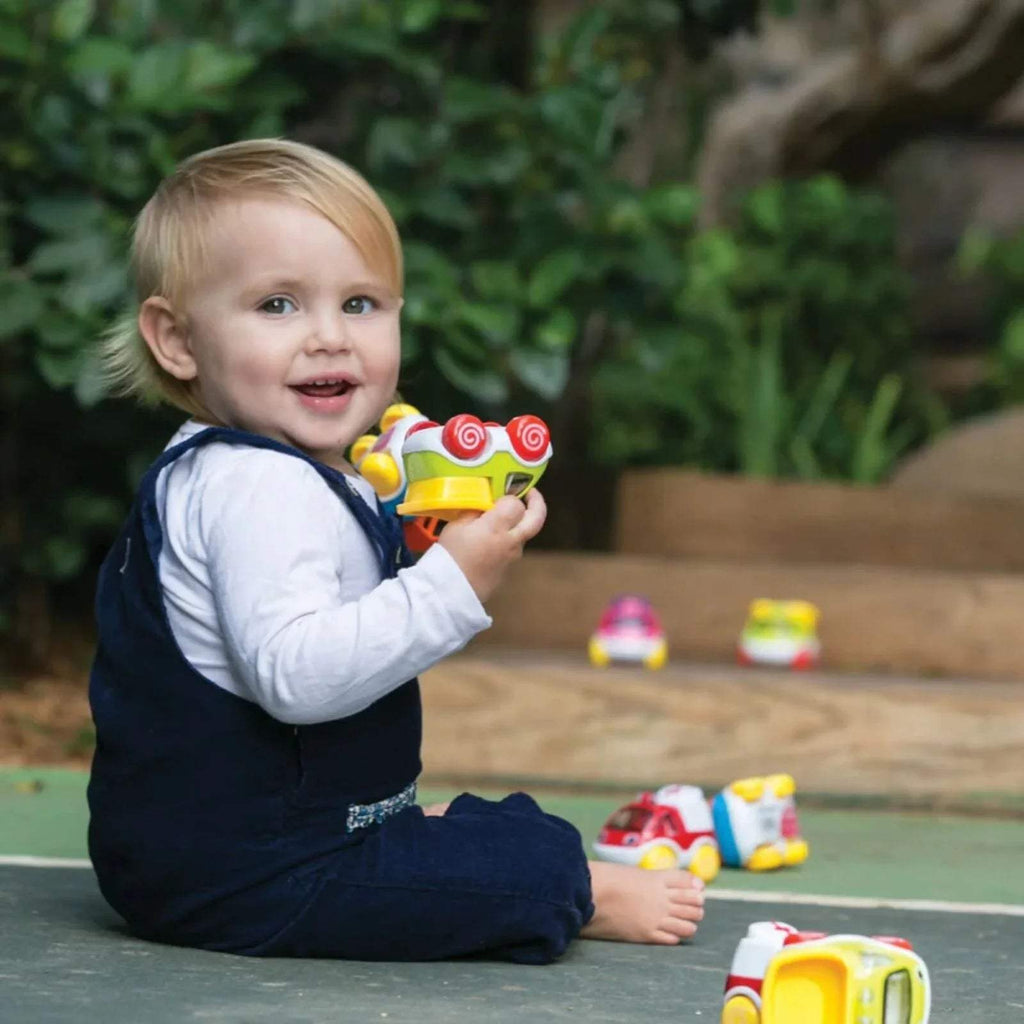 Yellow mini toy car with red swirl details, with other colorful cars on the floor