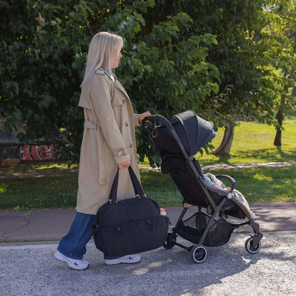 Black quilted shoulder bag hanging at side while walking with a stroller