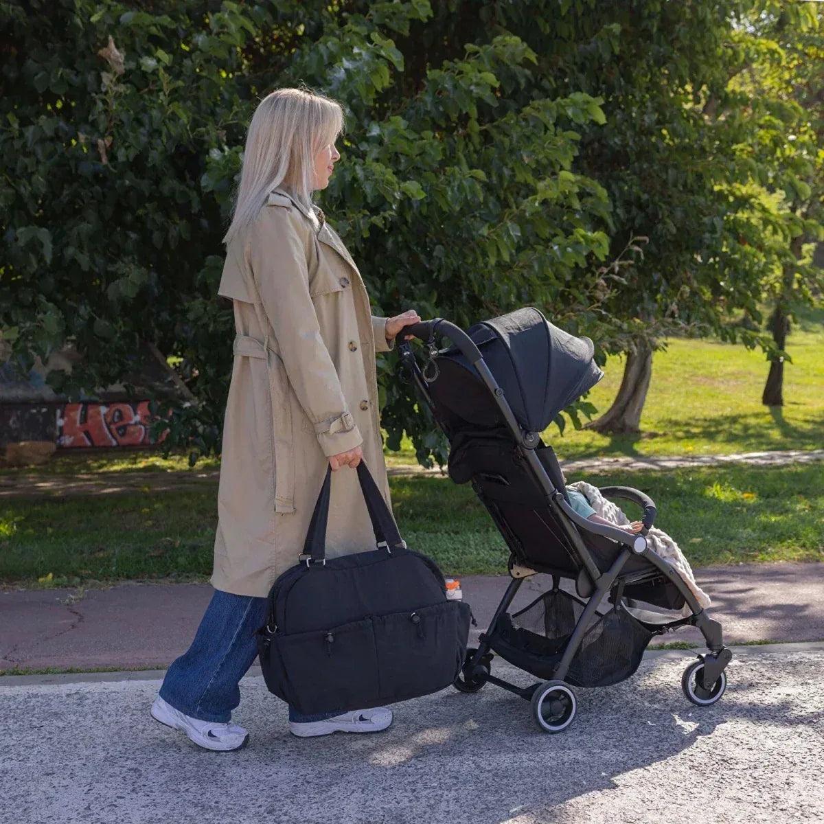 Black quilted shoulder bag hanging at side while walking with a stroller