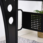 Black steel desk side frame with circular cutouts and integrated carry handle.
