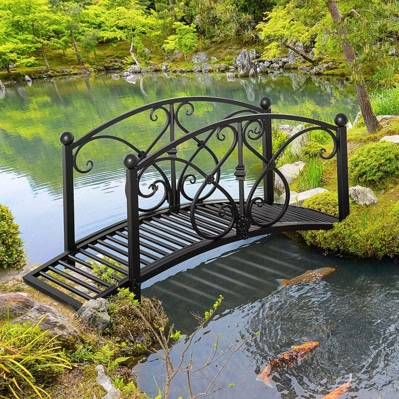 Black metal garden bridge over a pond or creek with arched railings and slatted deck