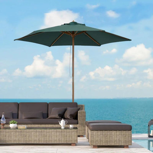 Outdoor patio set with a green umbrella and furniture against a blue sky and ocean background