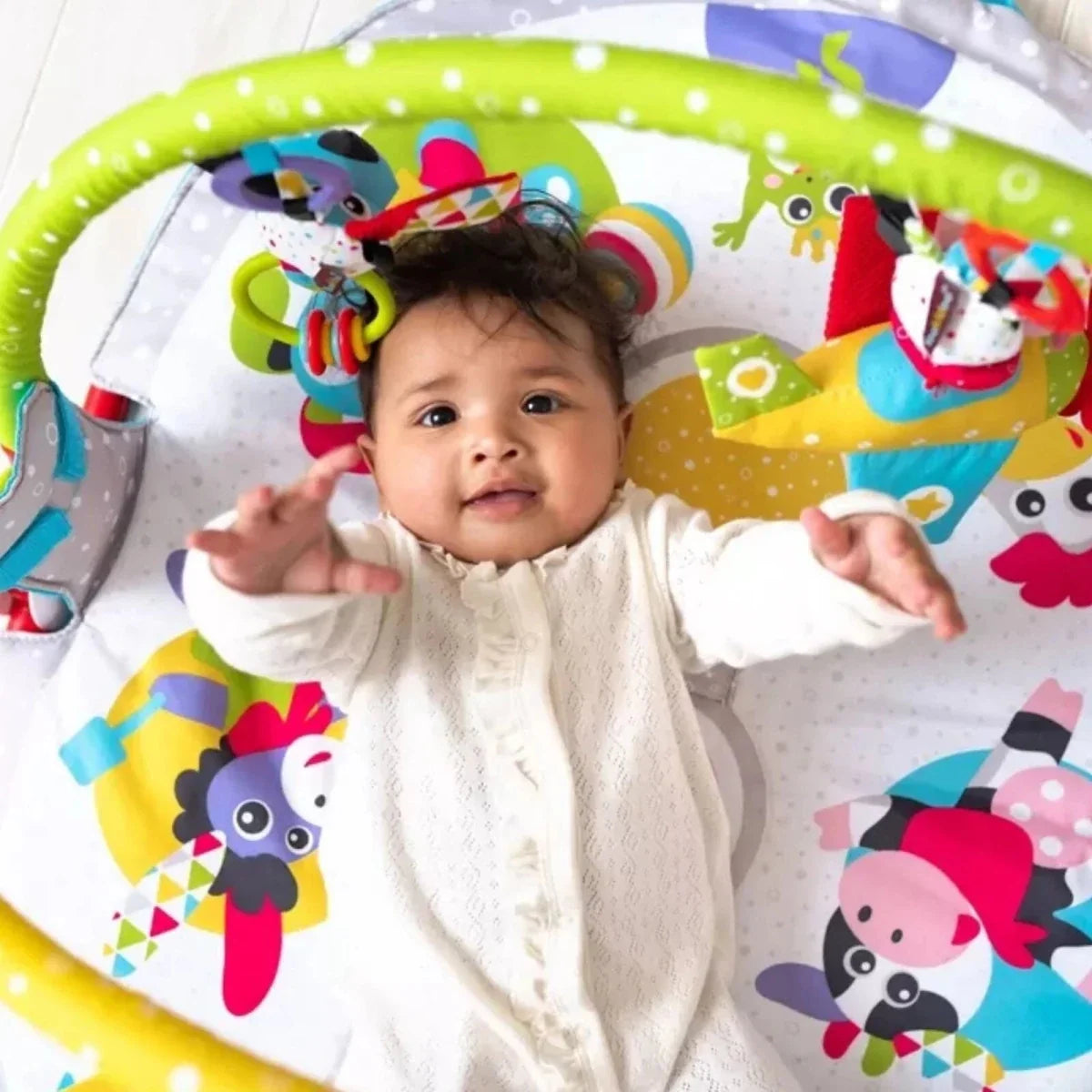 Baby lying on play gym mat with overhead arch and colorful hanging animal toys