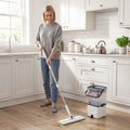 Woman mopping kitchen floor with flat mop head and white wringer bucket, gray pad