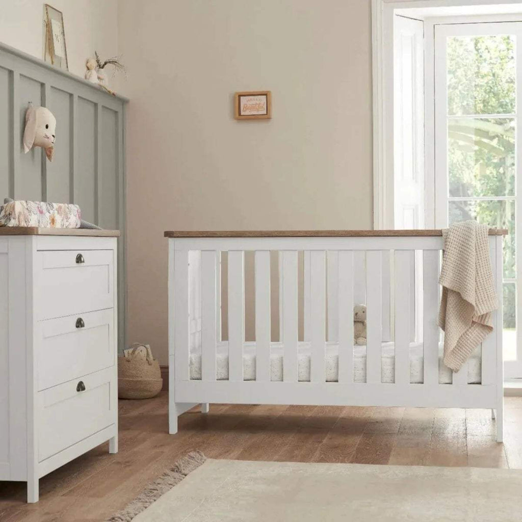 White wooden baby cot with vertical slats and raised mattress base