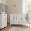 White wooden baby cot with vertical slats and raised mattress base