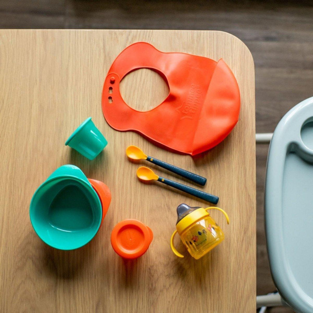 Silicone toddler bib, sippy cup, bowl, and weaning spoons on a table