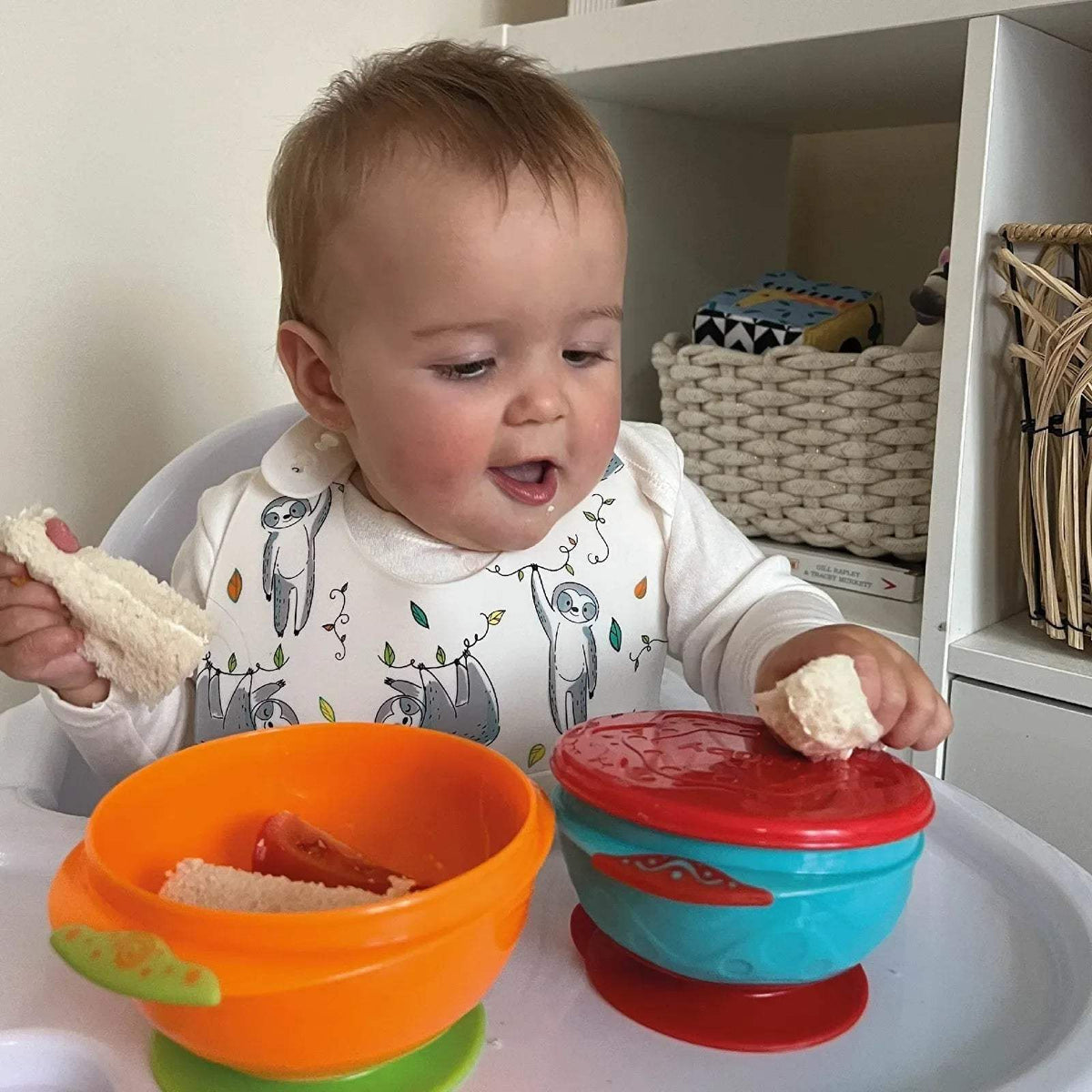 Stackable suction bowls in use: orange bowl and blue bowl with red lid in high chair