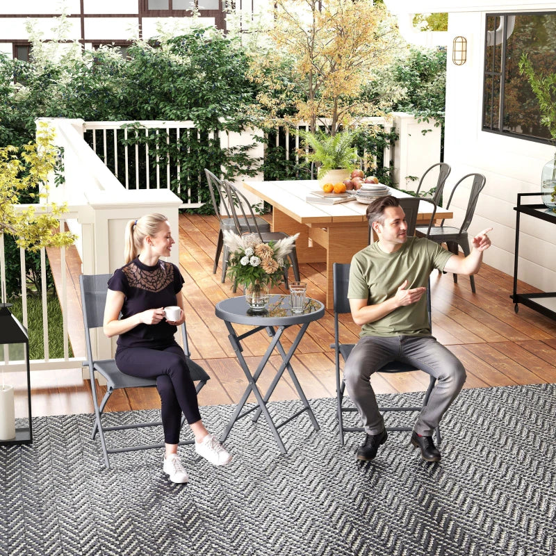 Grey outdoor bistro set with two folding chairs and round glass-top table outdoors