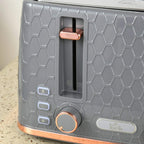 Grey toaster front with bread slots, indicator buttons, and browning dial, rose-gold trim
