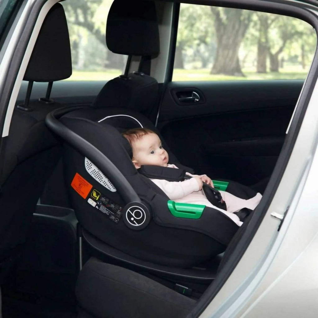 Black i-Size infant car seat installed in car, rear-facing with green handle accents
