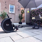 Black outdoor rowing machine placed on a patio next to a step and seating area.