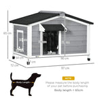 Grey wooden dog kennel with black roof and hinged front door, on four legs