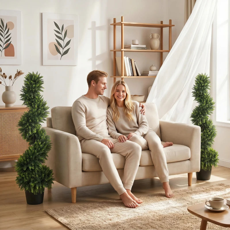 Two deep green artificial cypress trees in black pots beside sofa seating