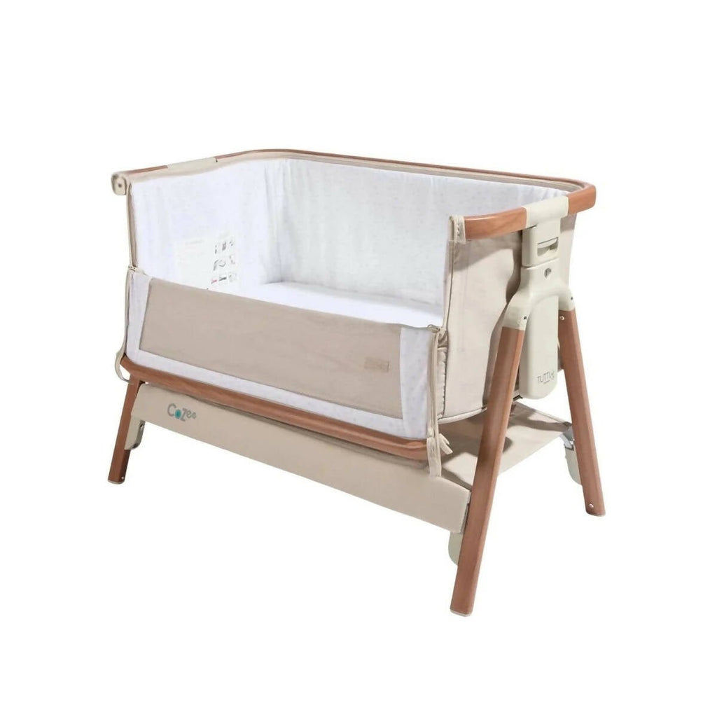 Angled view of ecru bedside crib with walnut frame and open padded side