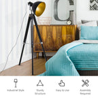 Tripod floor lamp with black frame and gold spotlight shade near a bed