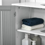Open grey under-sink cabinet showing shelves with folded towels and bottles.