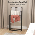 Black towel rail stand with three bars holding folded white towels and a pink cloth.
