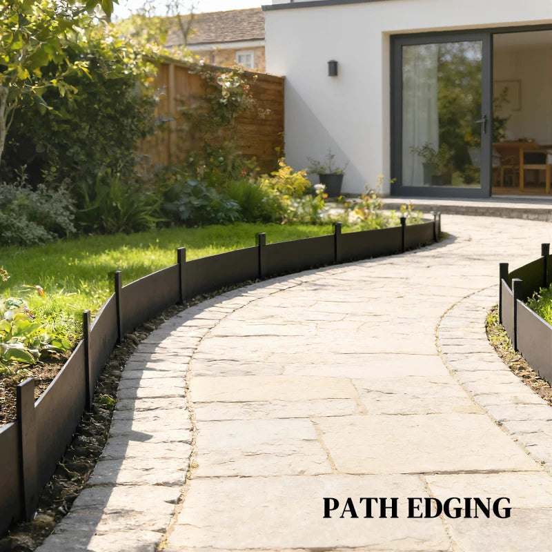 Black metal picket fence panel border along stone walkway in garden.