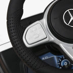 Black textured steering wheel with control buttons and pedals on white kids ride-on car