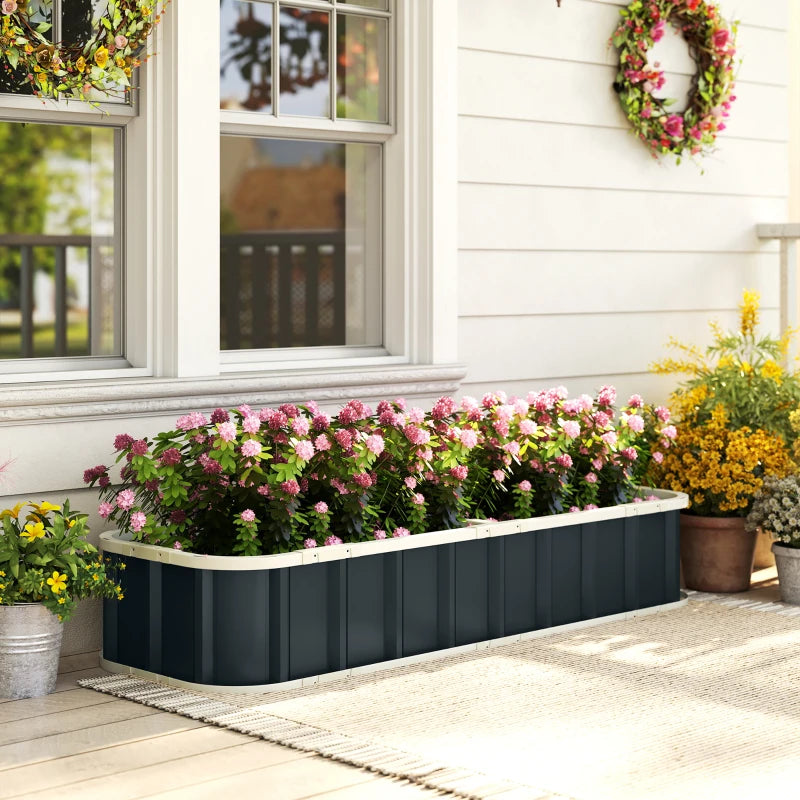 Dark grey raised garden bed with pink and yellow flowers beside a home walkway
