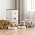 White automatic cat feeder with dual stainless bowls feeding a tabby and gray cat