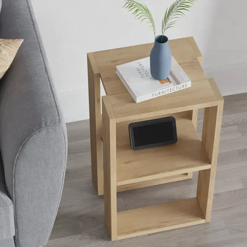 Light oak bedside table with open shelves and top surface, holding books and a vase.
