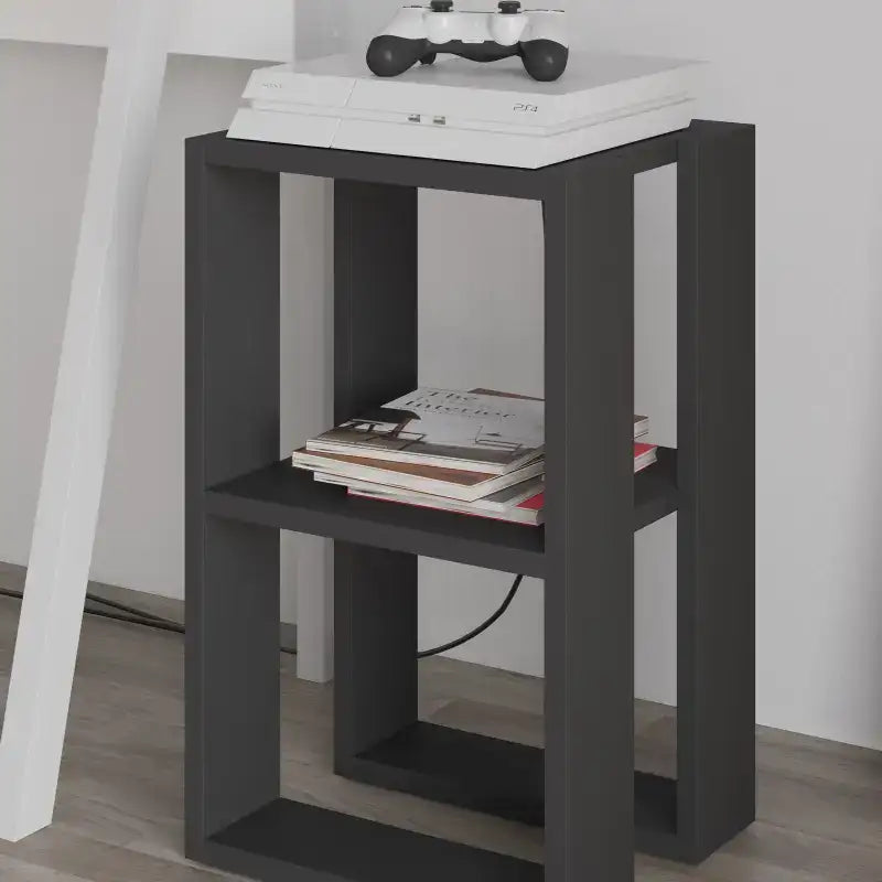 Modern bedside table with open shelves in dark charcoal, magazines and game console on top