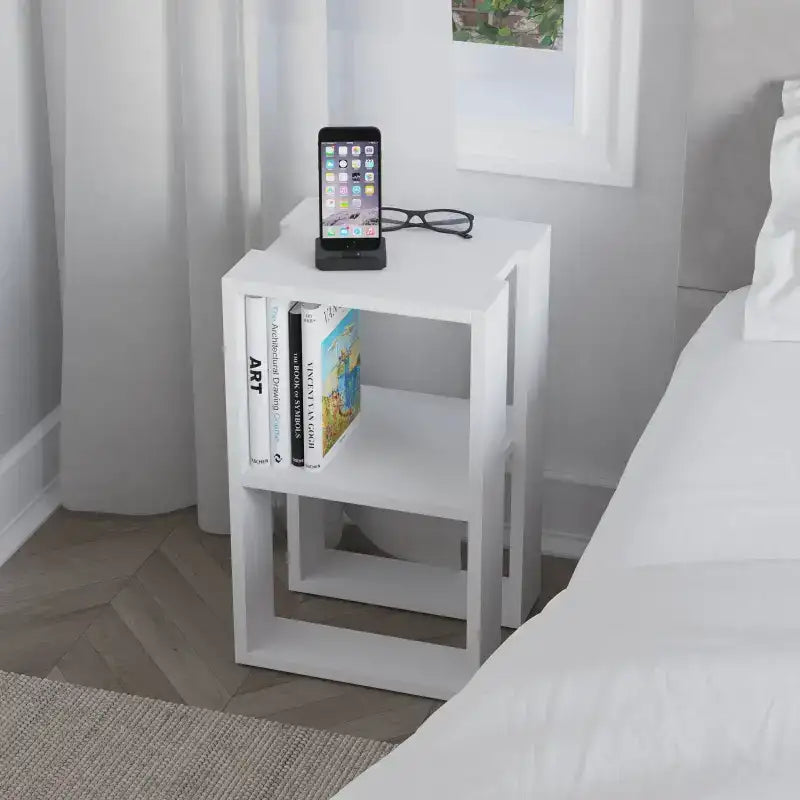 Modern bedside table with open shelves, white finish, holding phone and books